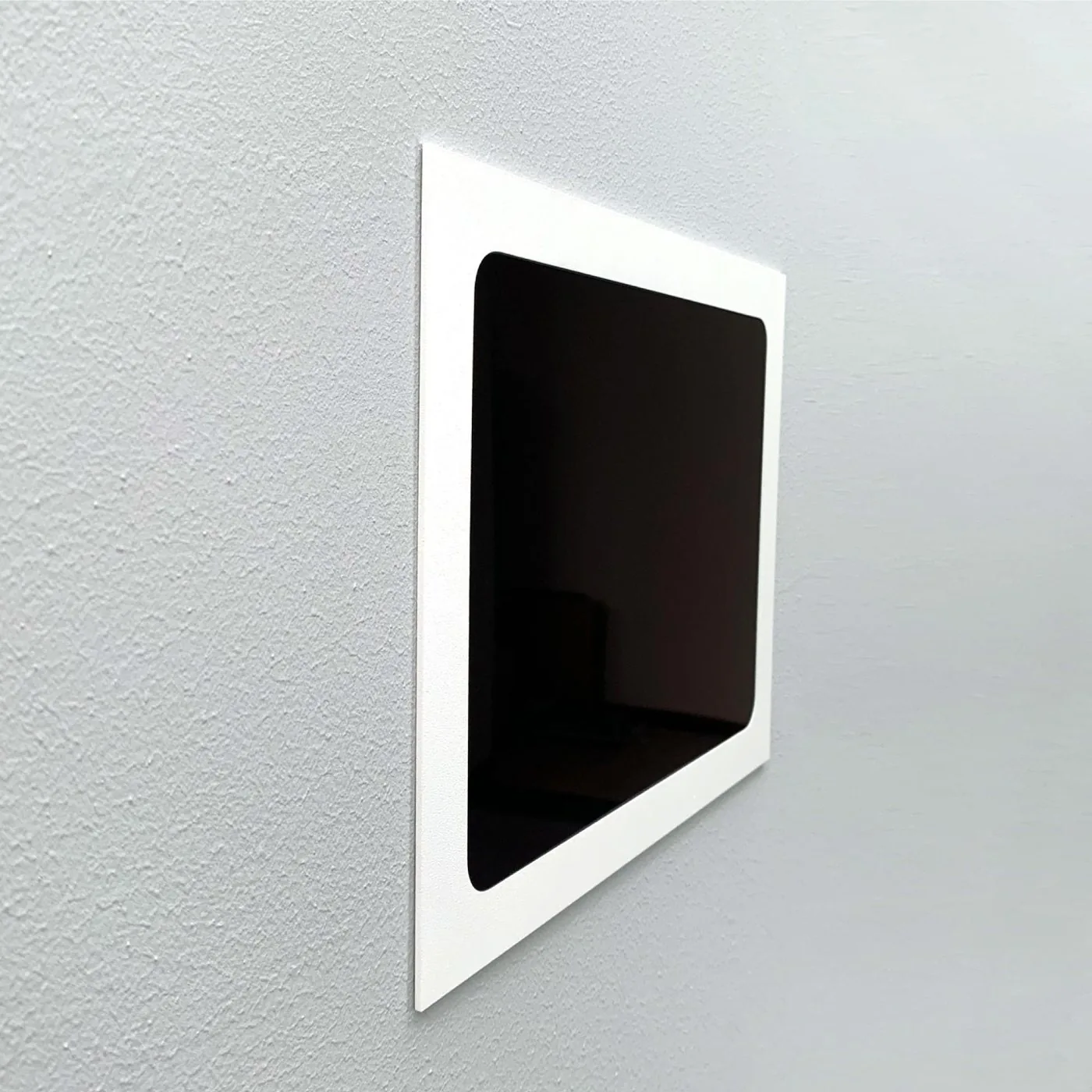 A white Whiz flush mount set into a textured grey wall, seen from an angle with the iPad screen off