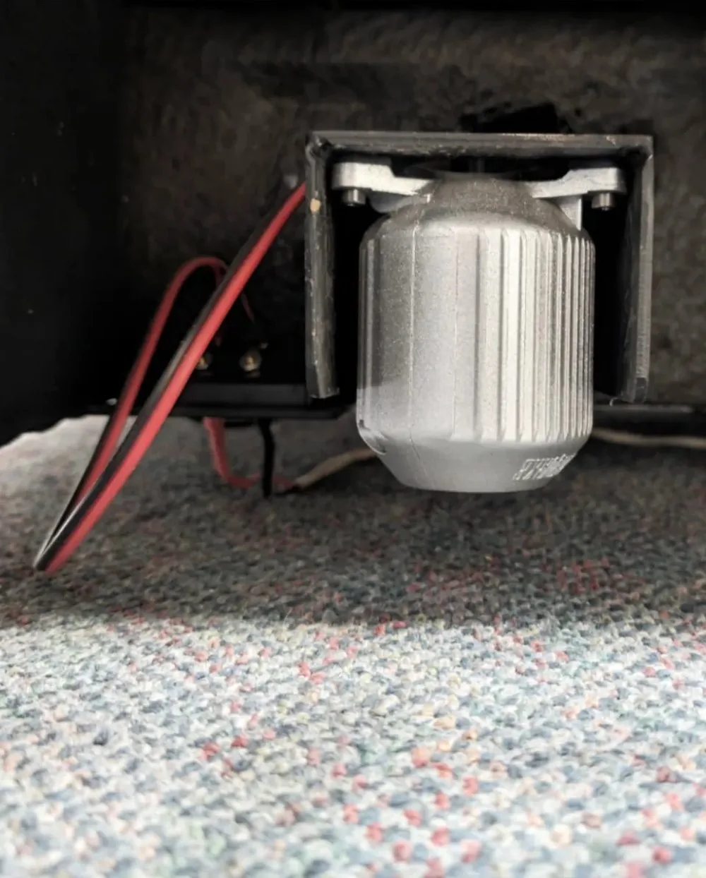 An Earthquake MQB-1 bass shaker mounted under a seat, with its wires run to the amplifier