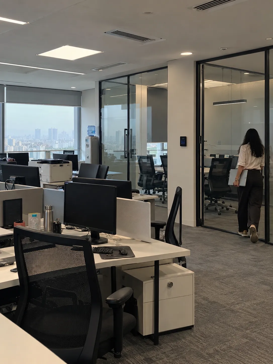 Open-plan office with a glass-walled meeting room, a KNX keypad beside its door and an employee walking in